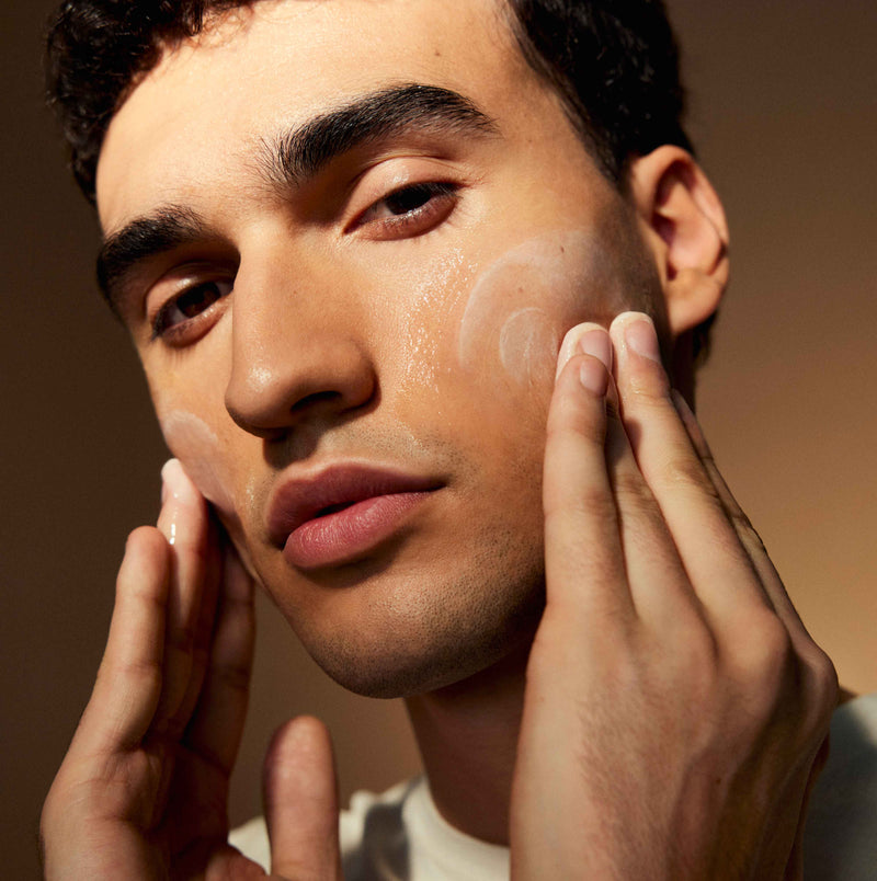 A man putting skincare product on both of his cheeks. 